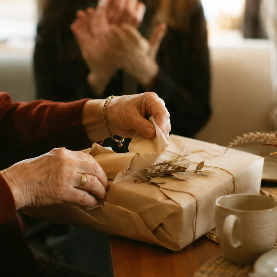 Mani che aprono un regalo incartato, circondate dai colleghi